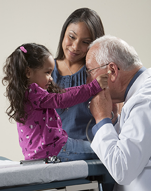 Healthcare provider playing with stethoscope with toddler girl while woman looks on.